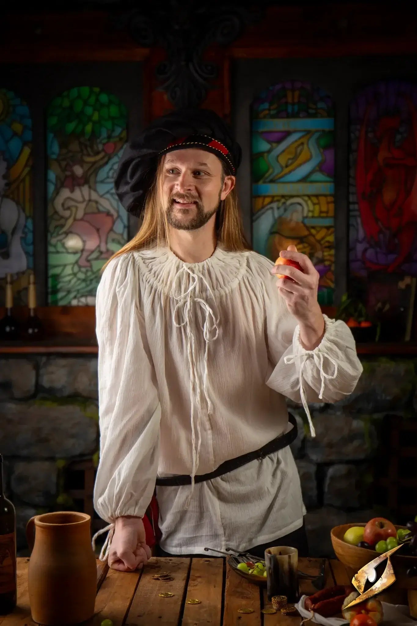Medieval man wearing a white shirt, holding an apple, standing in a rustic setting, showcasing versatile Shirts.