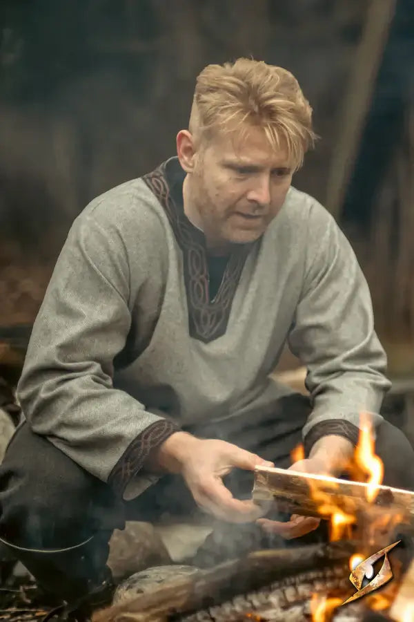 Man wearing a medieval tunic, sitting by a fire, embodying the spirit of medieval adventures.