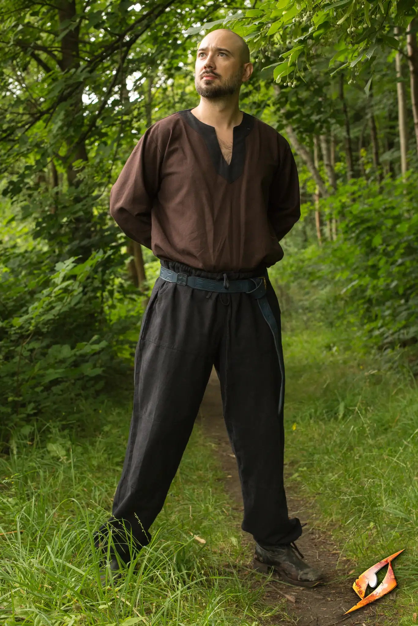 Man wearing Basic Pants and a brown tunic standing confidently in a lush green forest.