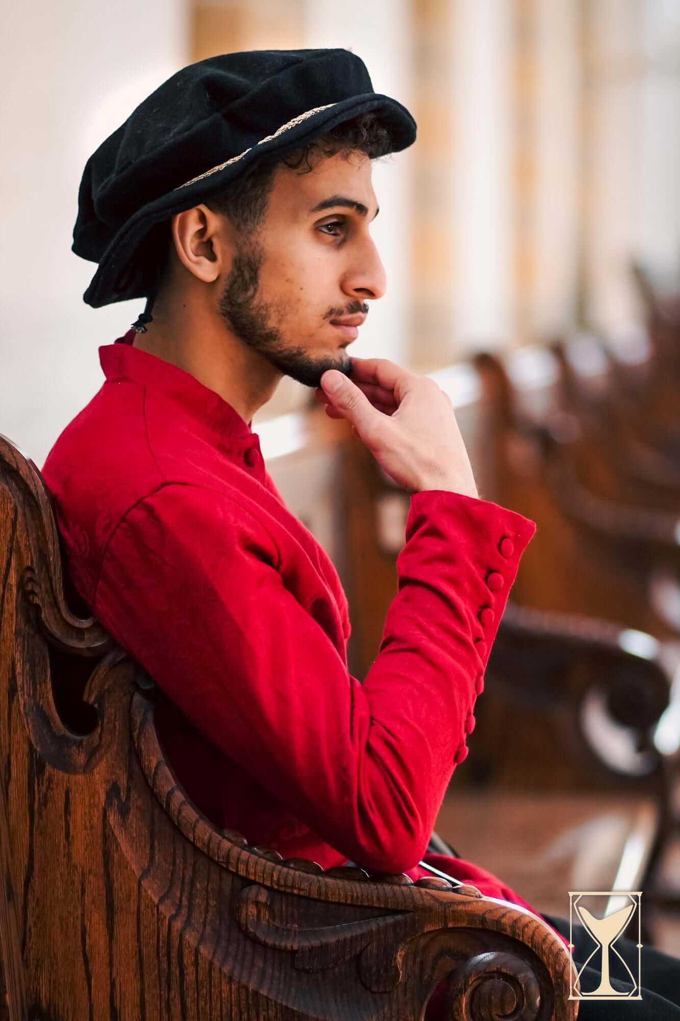 Flat Hat Edward worn by a model in a red outfit seated on a wooden bench, showcasing a historical look.