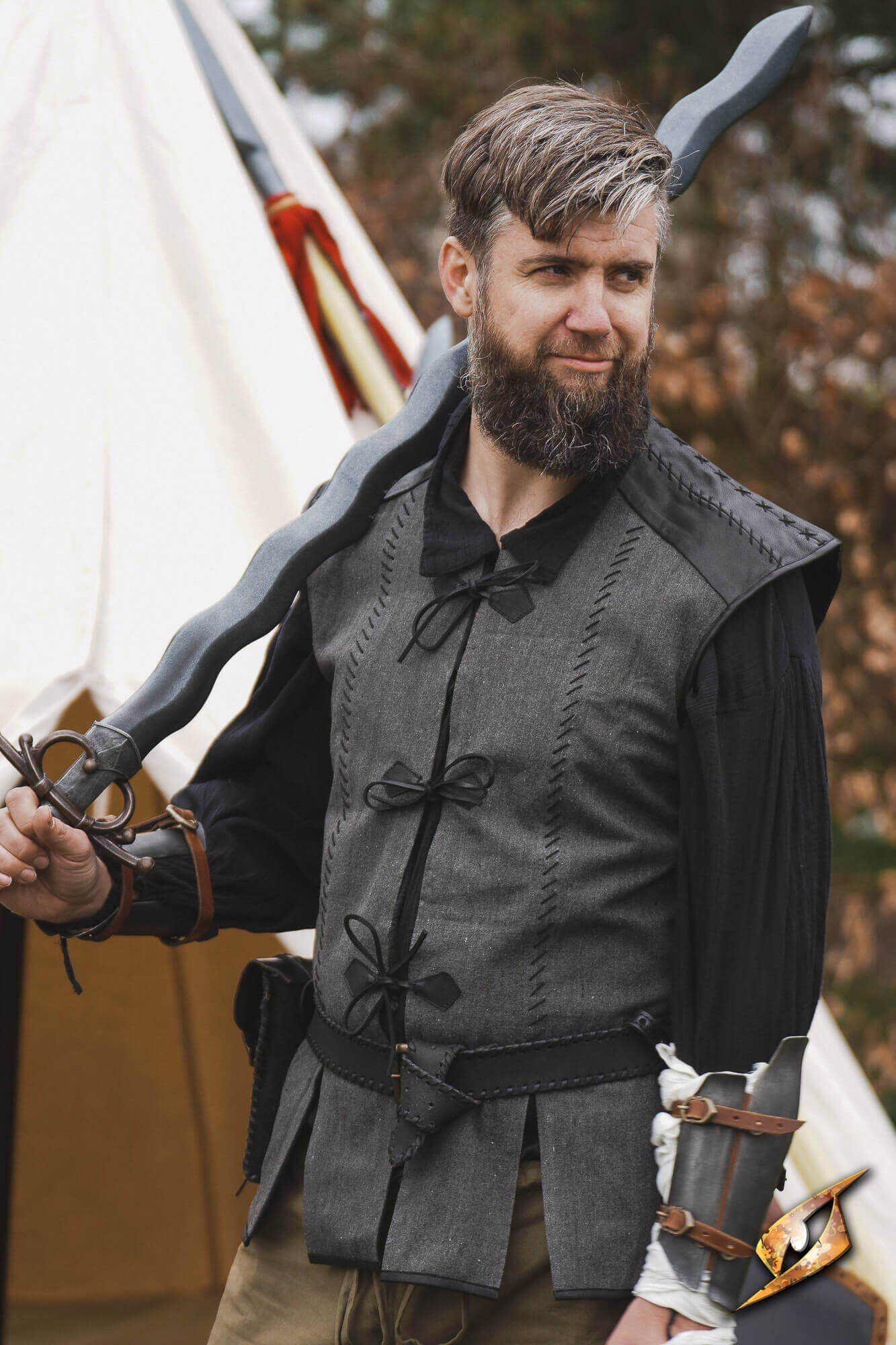 A man wearing a Rugged Canvas Jerkin, holding a sword, showcasing its utilitarian design and decorative stitching.