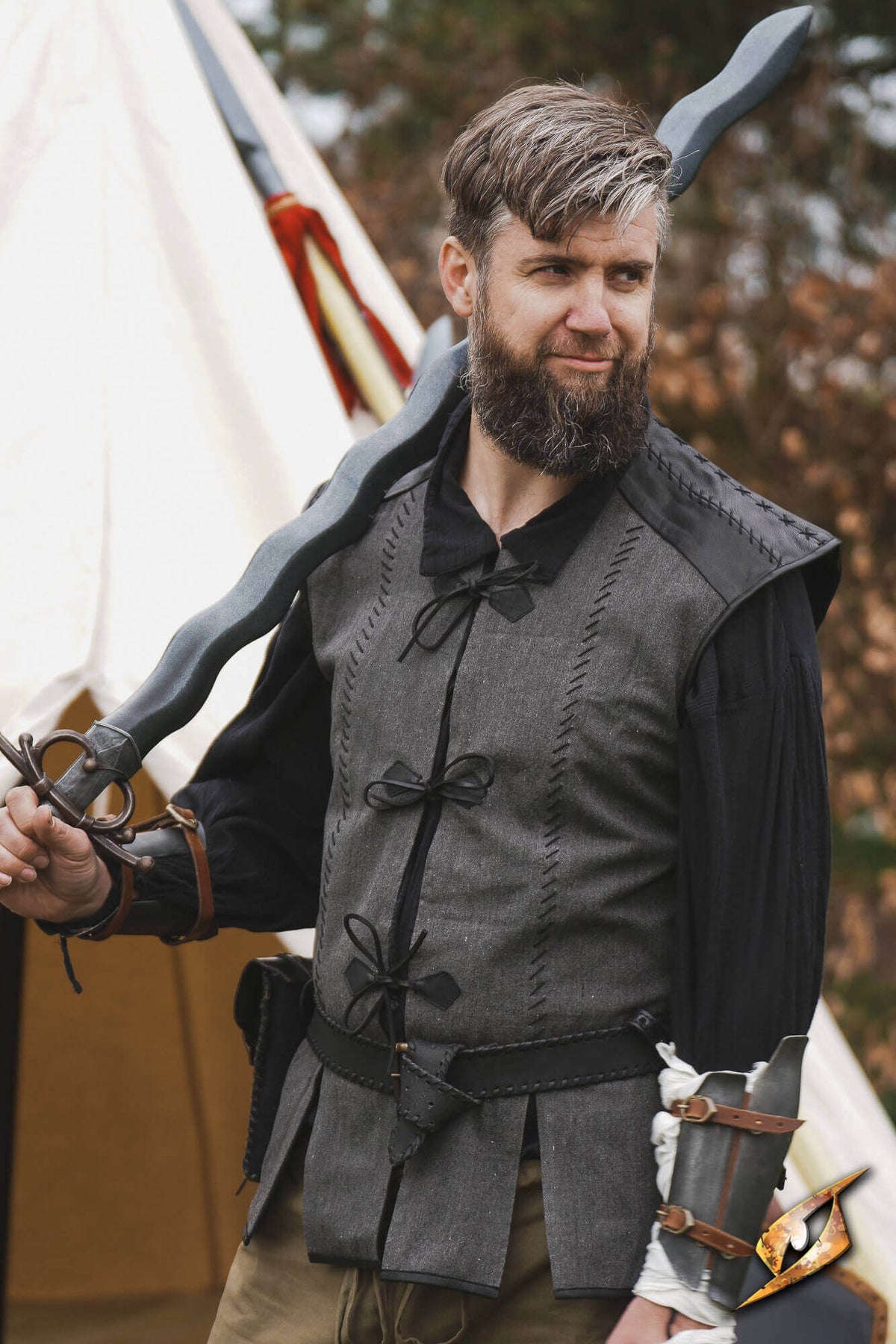 A man wearing a Rugged Canvas Jerkin, holding a sword, showcasing its utilitarian design and decorative stitching.