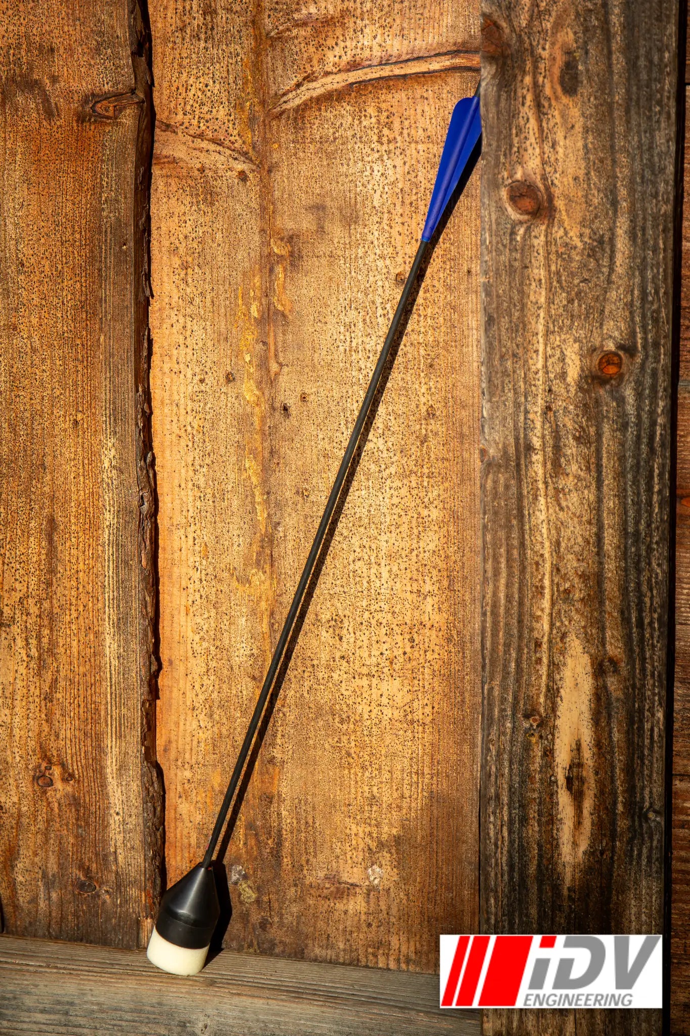 Arrow - Flat Head - Black Shaft leaning against a wooden wall, showcasing its sleek design and functionality.