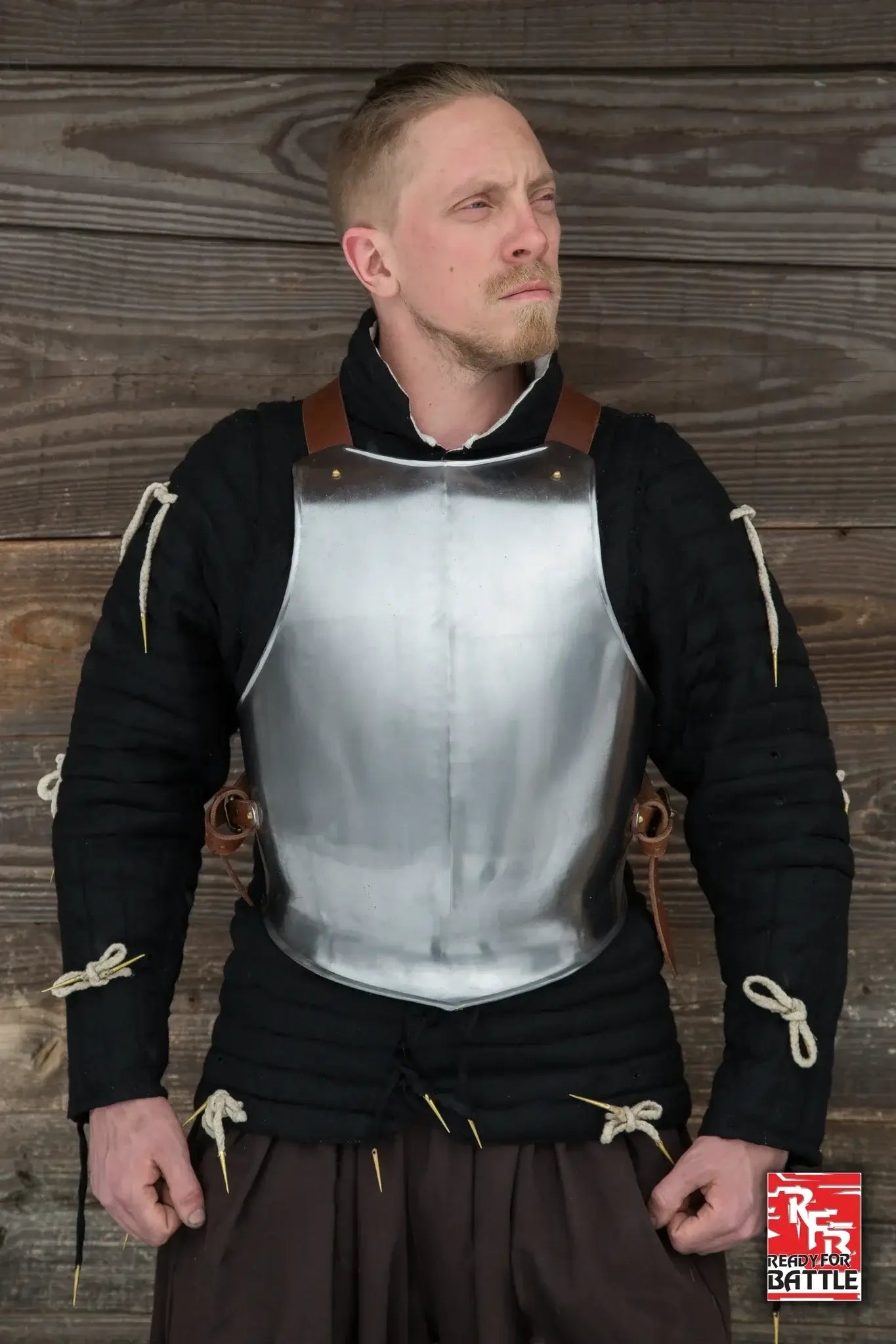 Knight wearing a medieval breastplate armor against wood backdrop, showcasing its design and protection features.