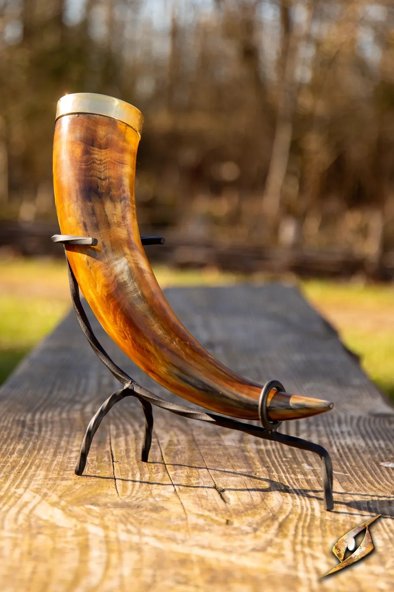 Brown drinking horn with golden trim on a wooden bench with a forest backdrop