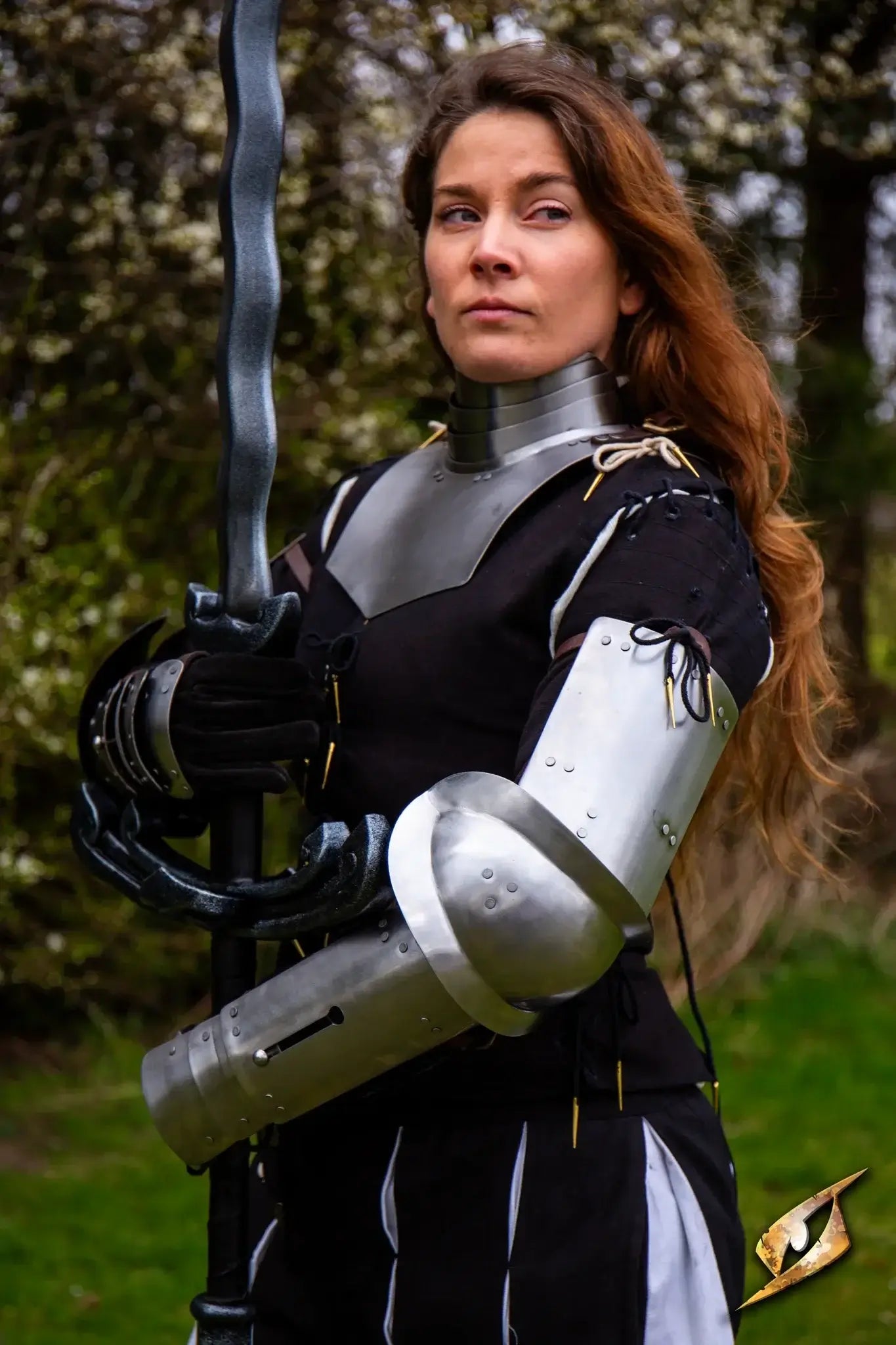 Woman in armort with a greatsword in hand, standing against a forestry backdrop