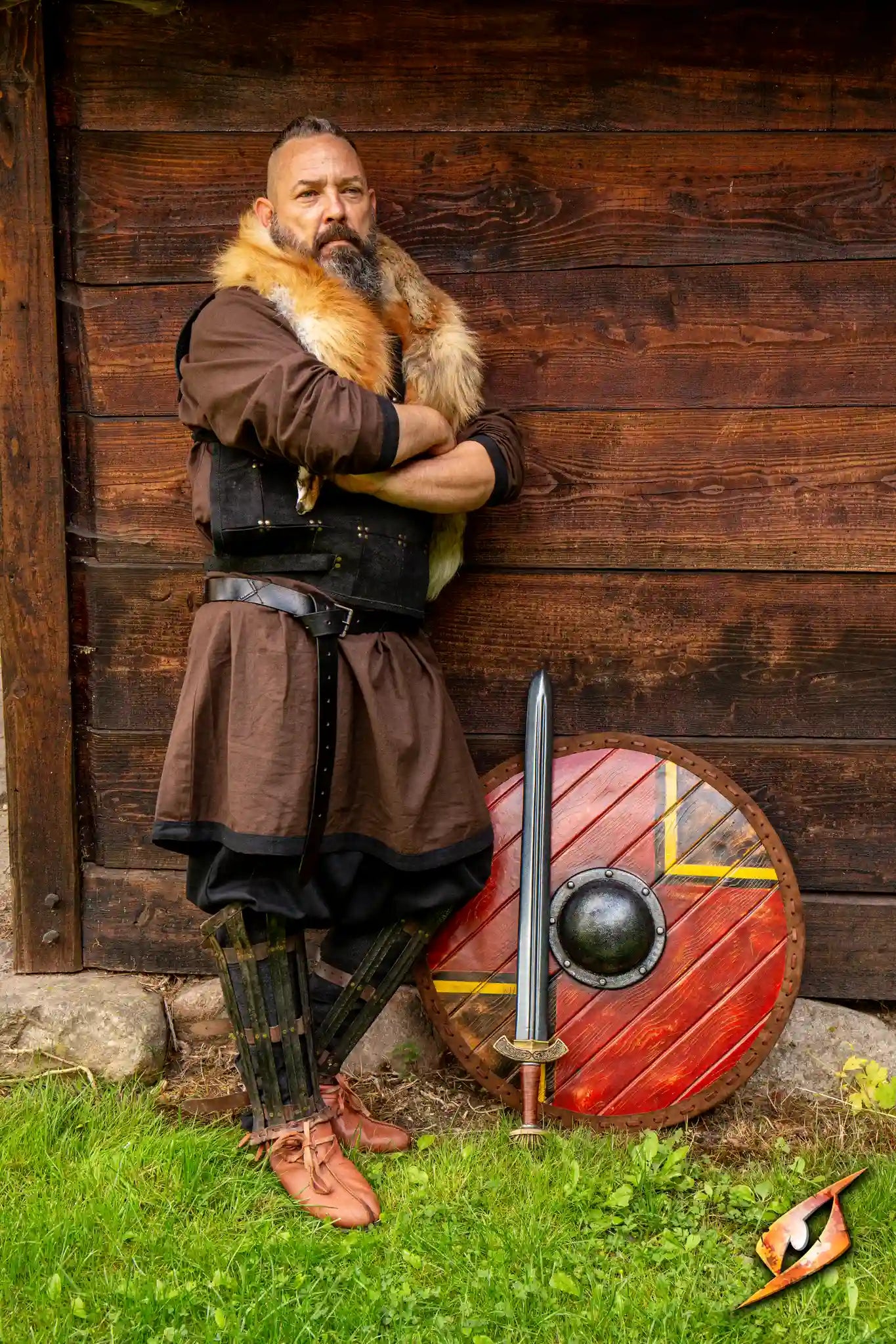 Person in viking clothing and armor leaning against a wooden structure with his sword and shield next to him