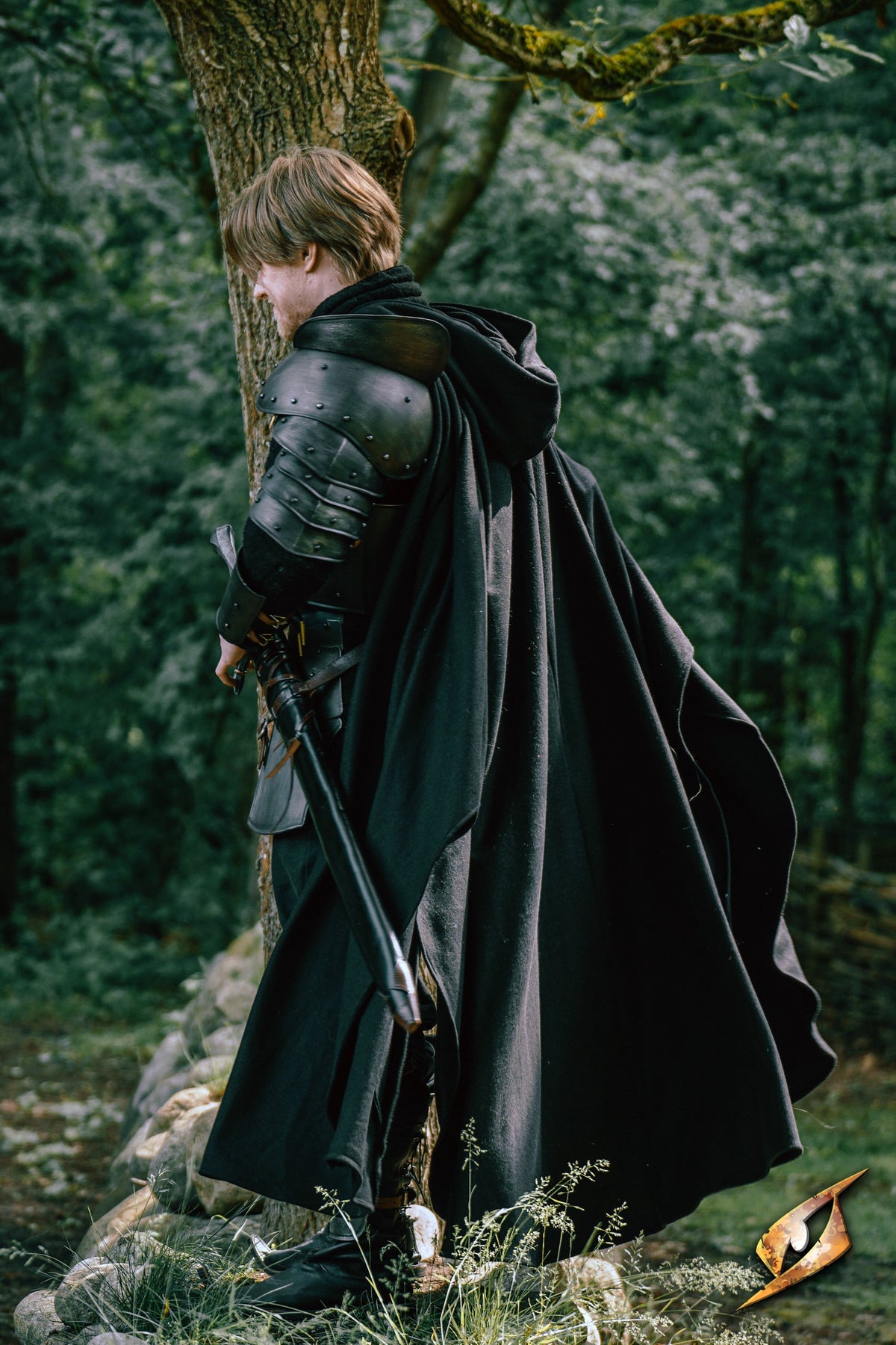 A child wearing a hooded Cape Godfrey Wool standing with a sword, set in a forested area.
