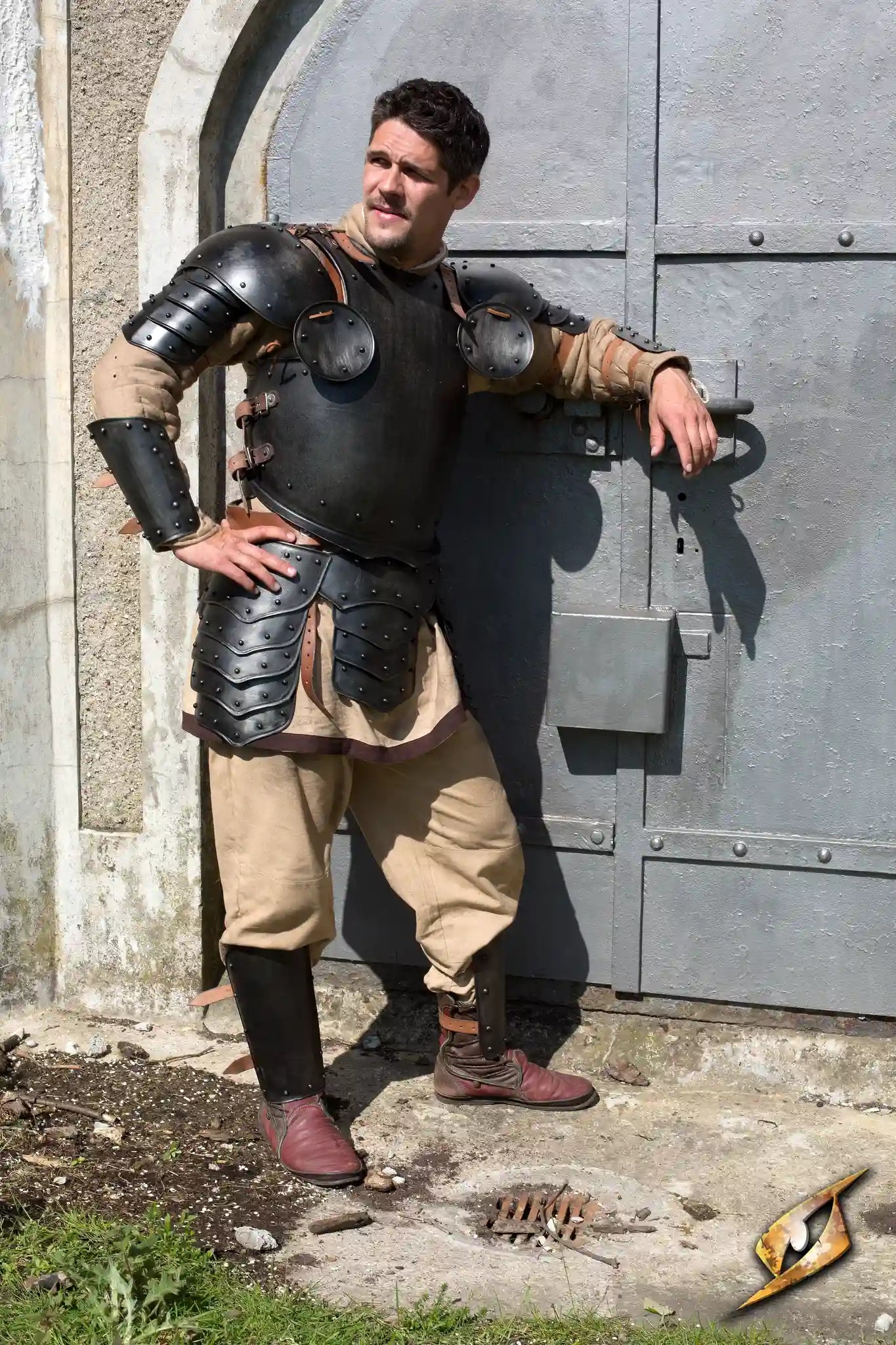 Warrior Complete Armour set worn by a man posing confidently in front of a medieval door with a dark color theme.