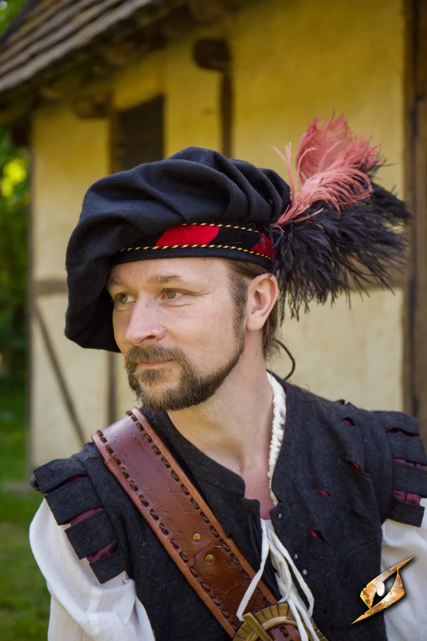 A man wearing a Wool Minstrel Hat with decorative feathers, standing outdoors near a rustic building.