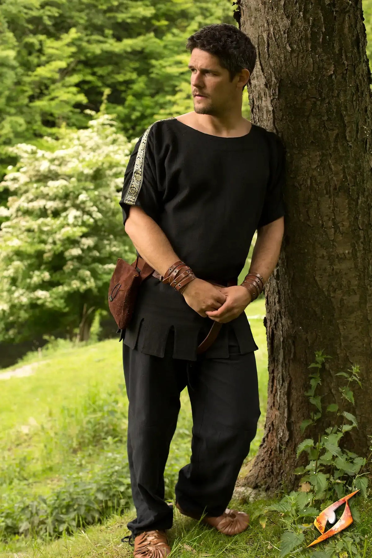 Roman Tunic worn by a man standing by a tree in a lush green outdoor setting.