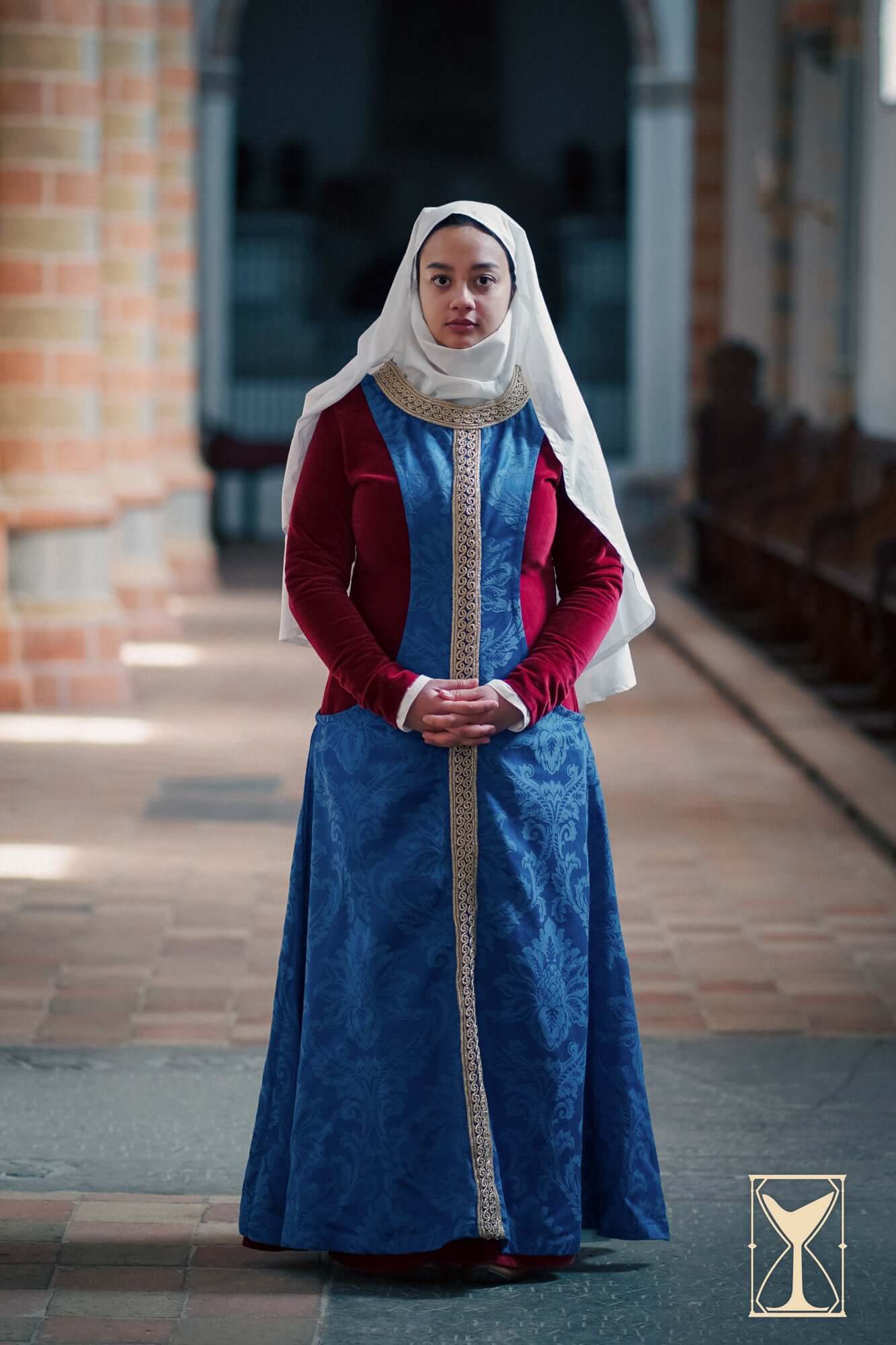 Pellote - Medieval Dress, a sleeveless surcoat in blue brocade, worn with a white veil and red sleeves, styled in a historical setting.