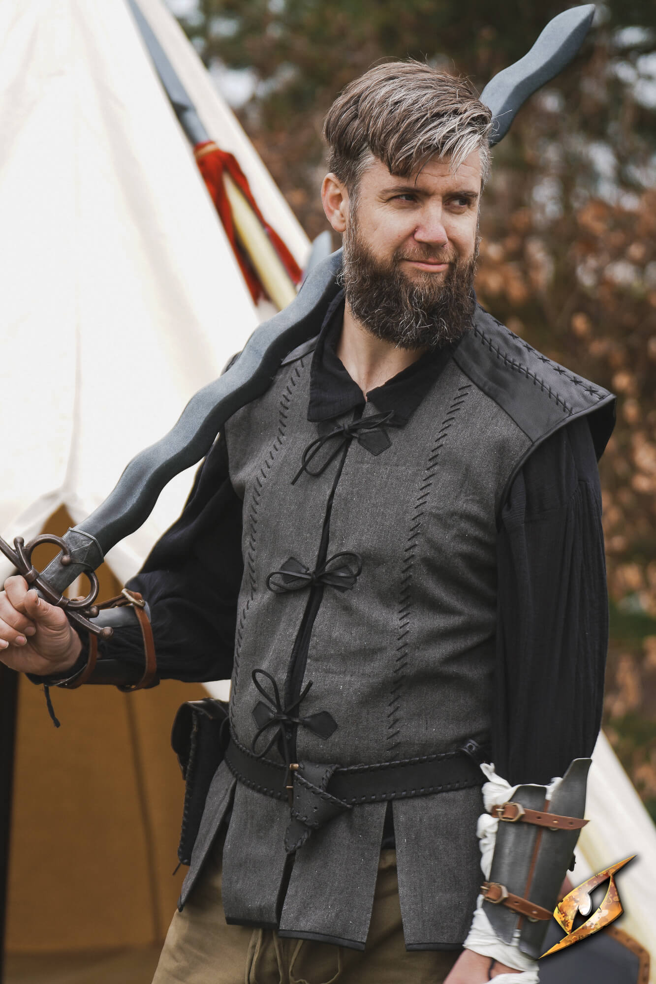 A man wearing a Rugged Canvas Jerkin, holding a sword, showcasing its utilitarian design and decorative stitching.