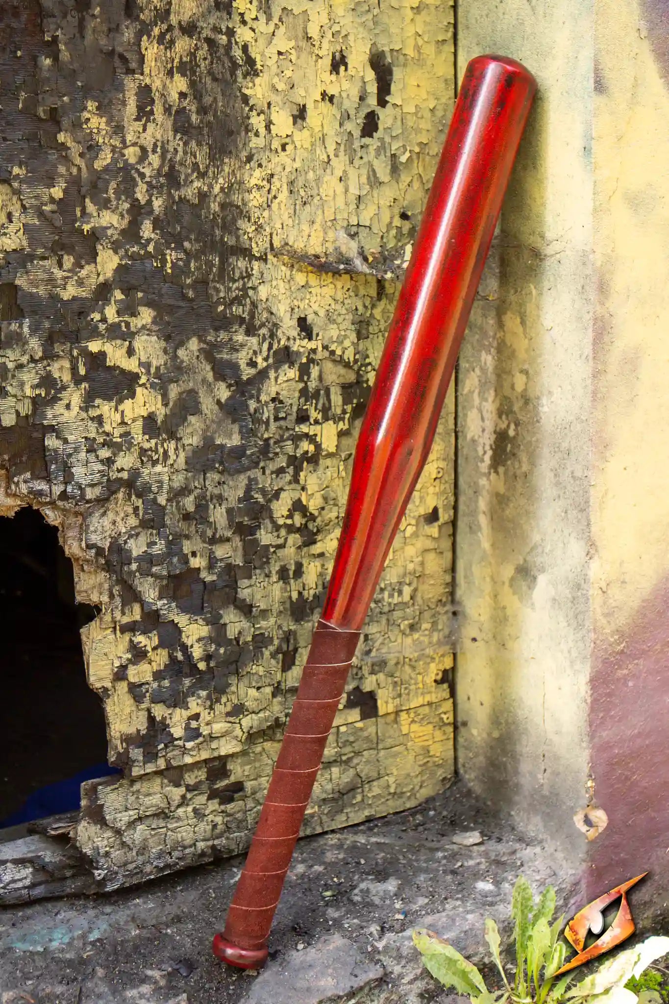 A red baseball bat leaning against a weathered, peeling wall in an abandoned location.