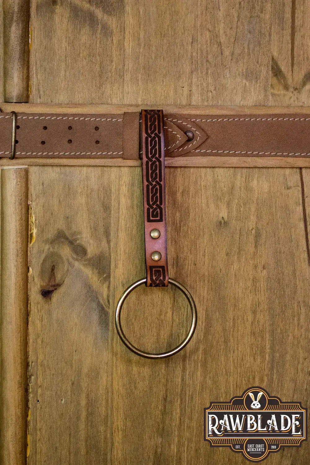 Runar Ring Holder with ornate leather design and a steel ring on a wooden background.