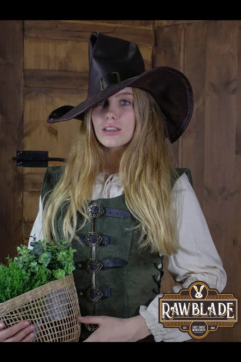 Wikka The Witch Hat worn by a model, brown leather hat with moldable wings, styled with a green vest.