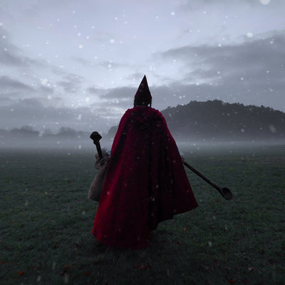 A elf in a deep red cloak walks in a misty open field, facing a dark forested hill. Snowflakes drift across as the sky glows in muted grey tones. The figure holds a long spoon and wooden staff, with a gnome hat on the head. In the full video version, an elf wearing Epic Armoury Illumine armor appears in the same wintry landscape, holding a elven Halbred.